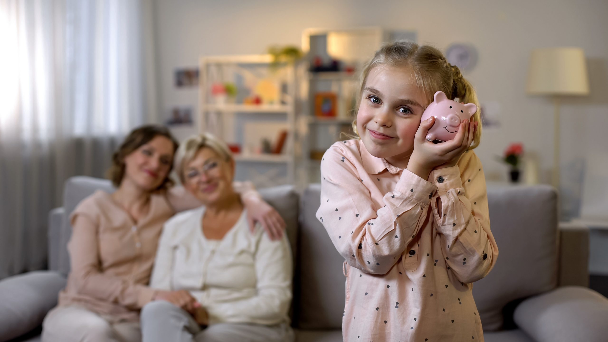 Daughter holding piggybank, mother and granny behind, teaching to save money