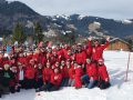 Gruppenbild mit winterlichen Hintergrund. Alle in roten Jacken und Mützen. Die Gruppe jubelt.