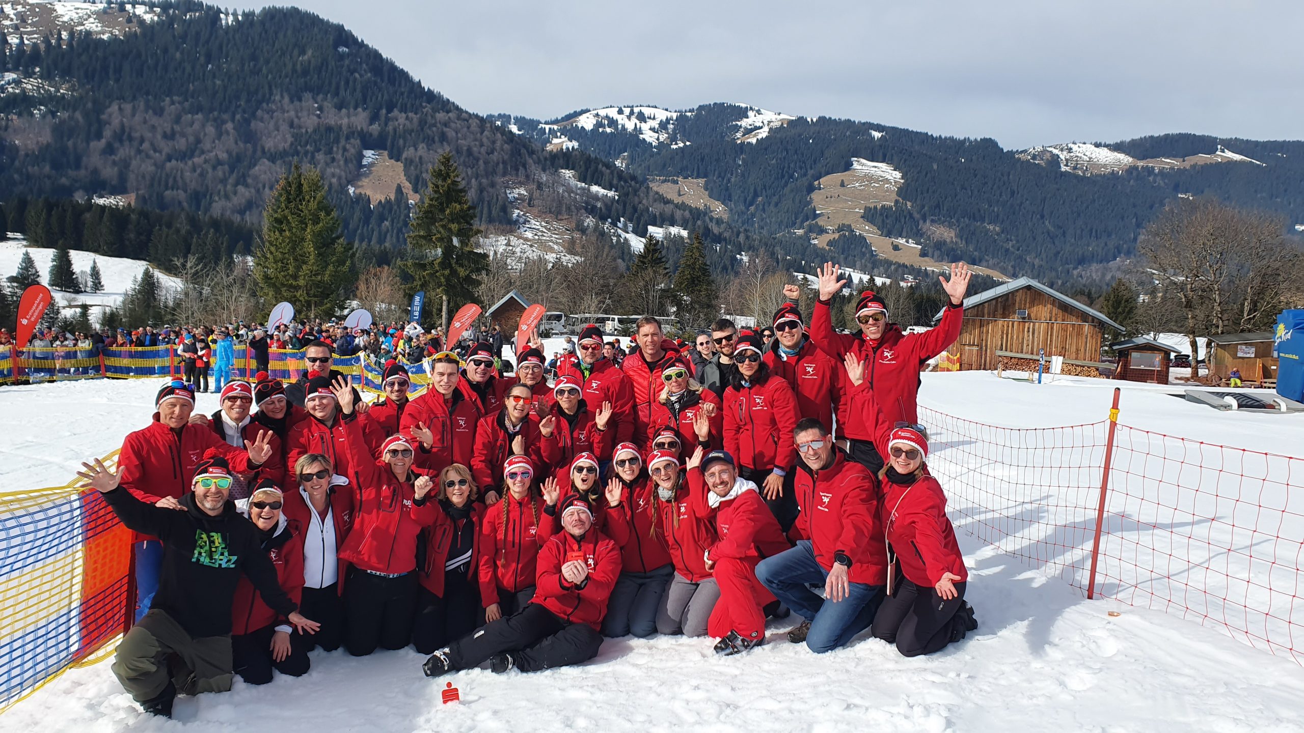 Gruppenbild mit winterlichen Hintergrund. Alle in roten Jacken und Mützen. Die Gruppe jubelt.