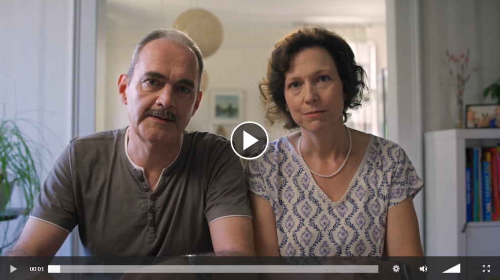 Videoausschnitt eines Ehepaars. Dieses schaut besorgt in die Kamera. Das Ehepaar sitzt in einem Wohnzimmer.