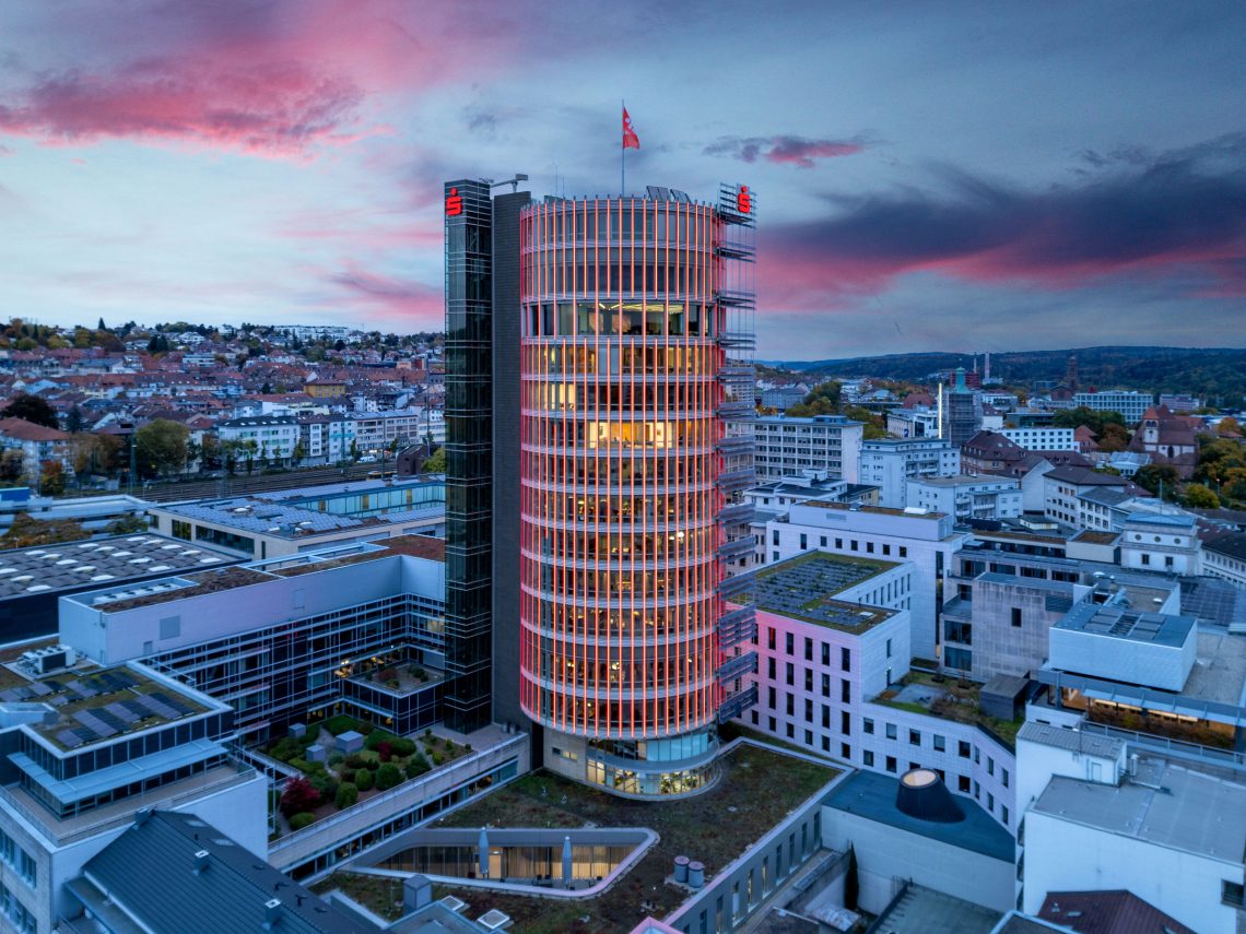 Der Sparkassenturm in der Abenddämmerung. Leichte lila Wolken. Der Turm strahlt rot. Vereinzelt sind noch beleuchtete Büros zu erkennen.