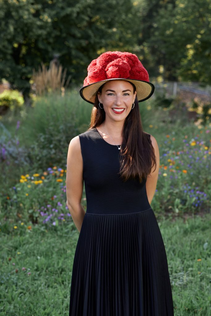 Alicia Lindner steht vor einer schönen Blumenwise. Sie trägt ein schwarzes Kleid und einen Schwarzwälder Bollenhut. 